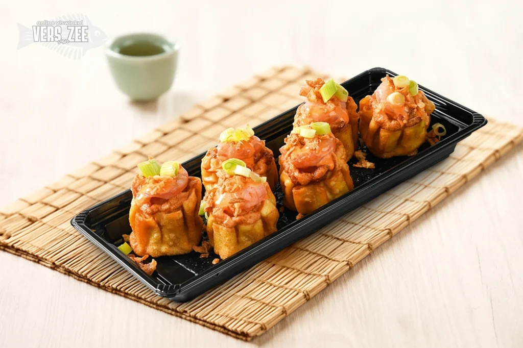 Vijf gefrituurde open dumplings met zalm en garnituur van bosui in zwarte tray, geserveerd op een bamboemat met groene theekop op lichte ondergrond.